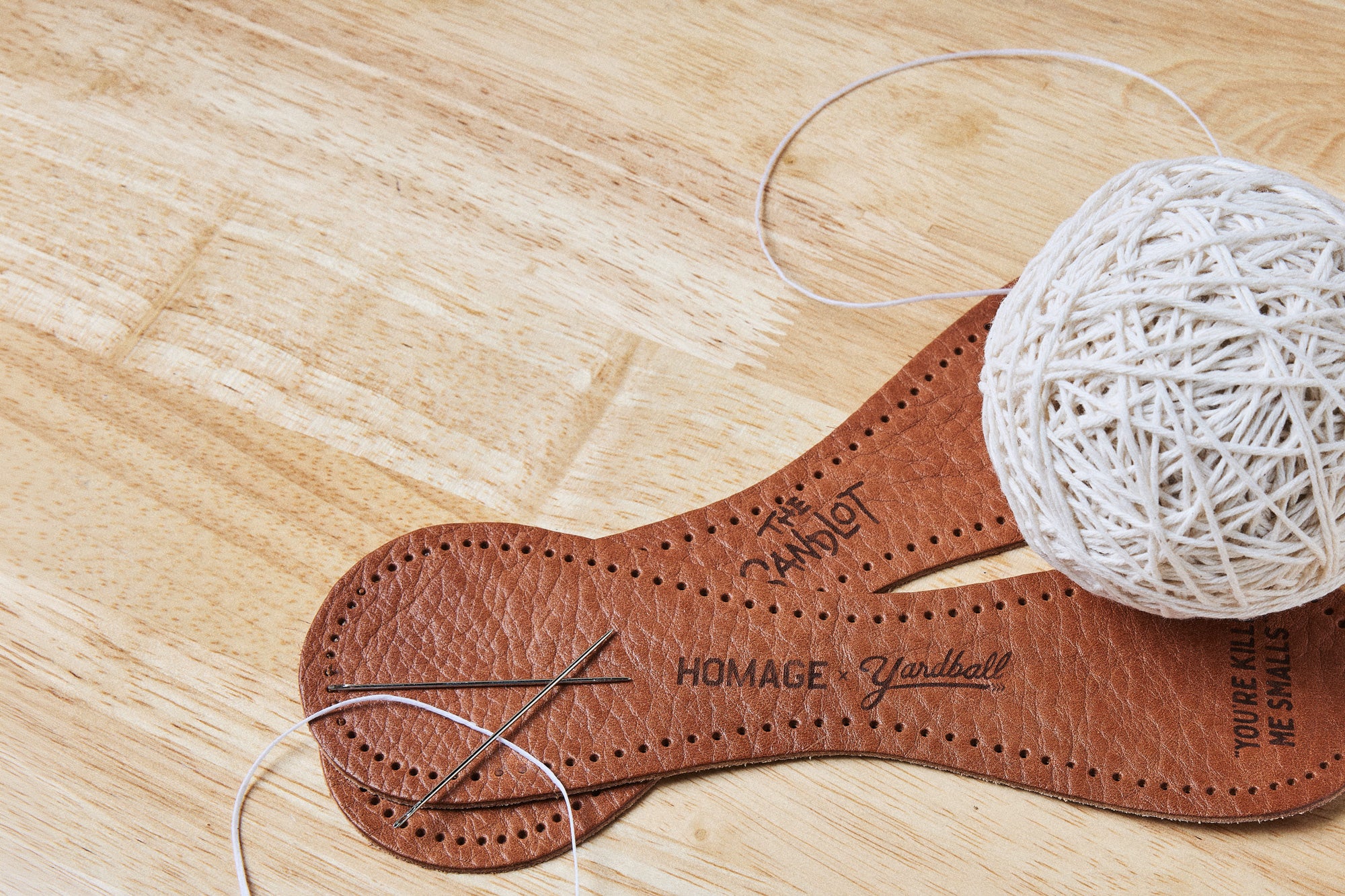 Homage by Yardball leather catch-ball panels being hand-stitched, with needles and a ball of thread on a wood bench.