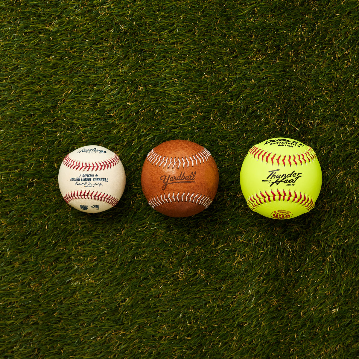 A baseball, a Yardball and a softball side by side on grass, seen from above